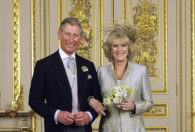 Oficiali vestuvinė nuotrauka. Į koplyčią Camilla įžengė pasipuošusi „Robinson Valentine“ sukurtu žemę siekiančiu elegantišku aukso siūlais siuvinėtu pilkšvos spalvos apsiaustu, po kuriuo slėpėsi lengva porceliano žydrumo suknelė / Getty nuotrauka